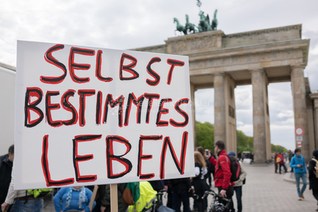 Ein Protest vor dem Brandenburger Tor in Berlin. Im Mittelpunkt ist ein Banner. Auf dem Banner steht: Selbstbestimmtes Leben.