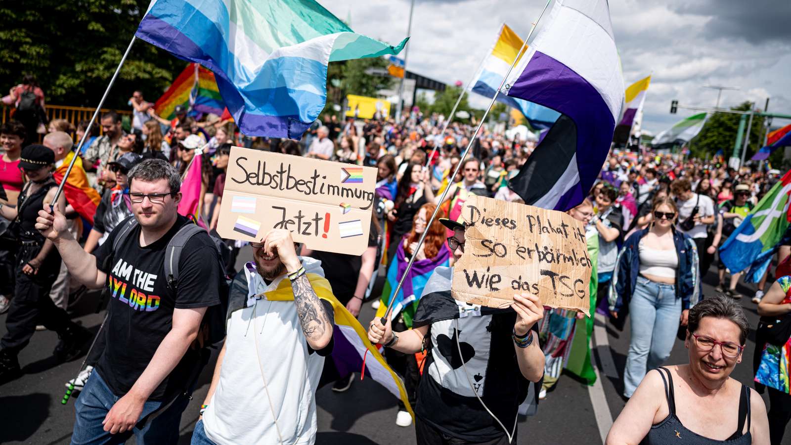 Auf einer Demo halten Menschen Fahnen und Banner hoch. Auf dem Banner steht: Selbstbestimmung jetzt.